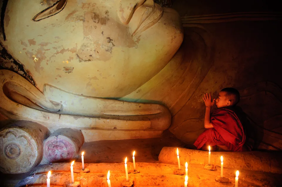Junger Mönch betet vor einer liegenden Buddha-Statue im Kerzenlicht
